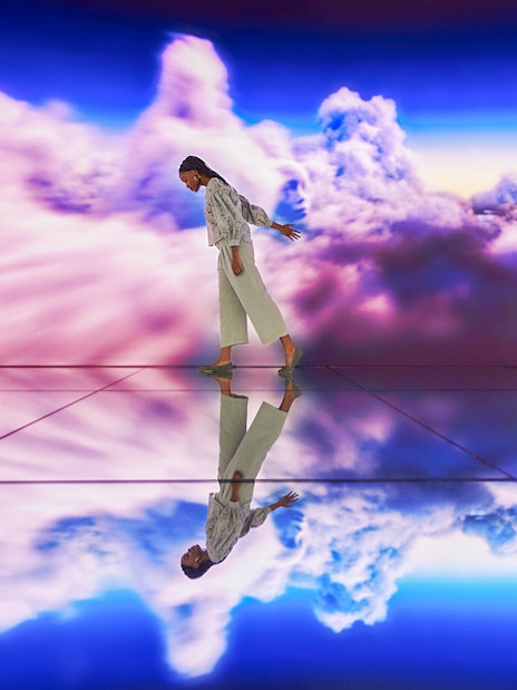 Person walking on reflective floor with vibrant cloud backdrop.