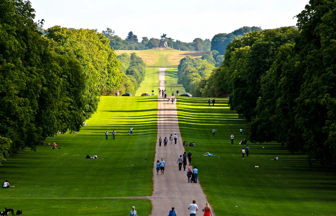 People walking along the Long Walk in Windsor, lined with trees, leading to the Copper Horse statue.