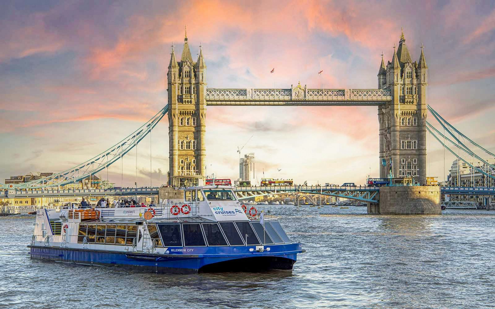 Dinner cruise boat on the Thames River passing by Tower Bridge at sunset.