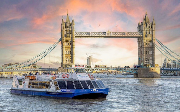 Dinner cruise boat on the Thames River passing by Tower Bridge at sunset.