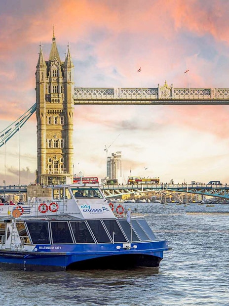 Dinner cruise boat on the Thames River passing by Tower Bridge at sunset.
