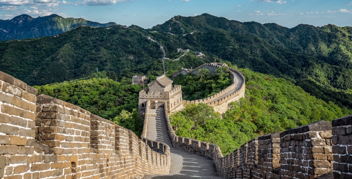Great Wall of China winding through lush green mountains under a blue sky.