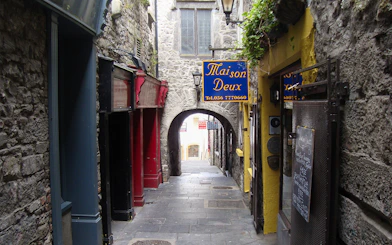 Narrow stone alleyway in Kilkenny with colorful shop signs and archway.