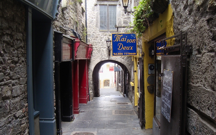 Narrow stone alleyway in Kilkenny with colorful shop signs and archway.