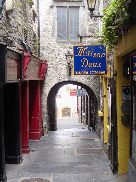 Narrow stone alleyway in Kilkenny with colorful shop signs and archway.