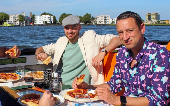 People enjoying pizza and drinks on an Amsterdam canal cruise.