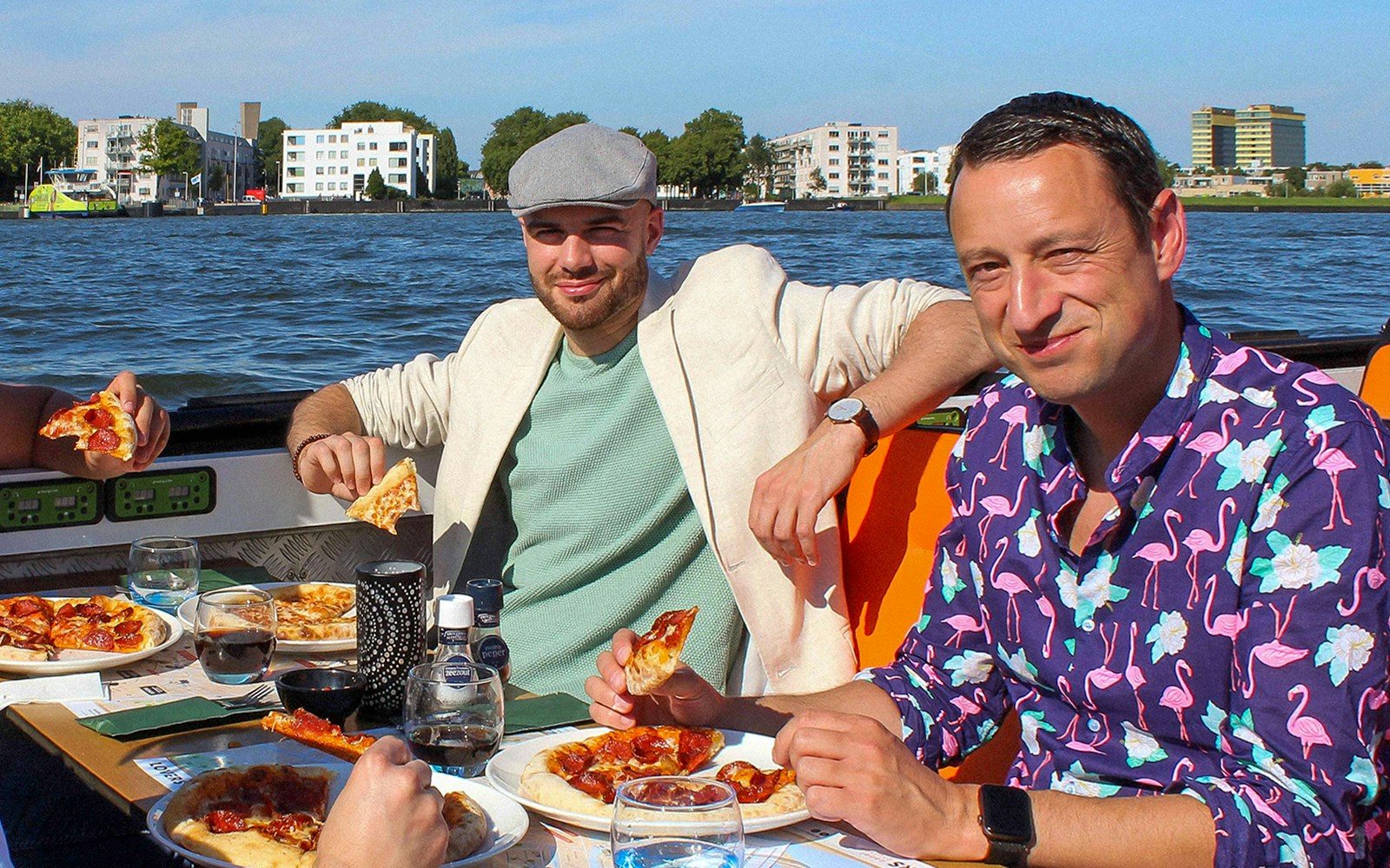 Amsterdam canal cruise with passengers enjoying pizza and drinks at sunset.