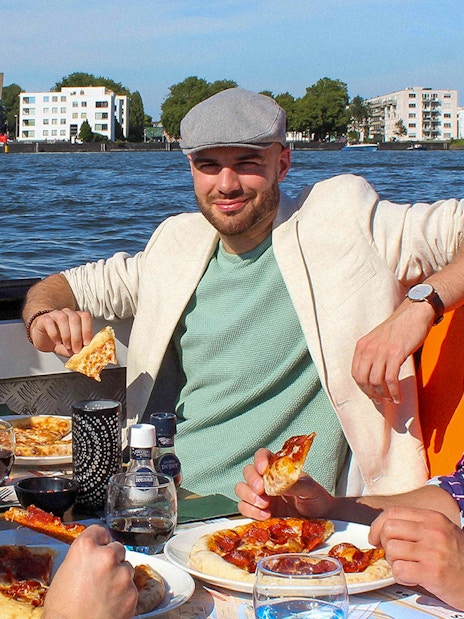 People enjoying pizza and drinks on an Amsterdam canal cruise.