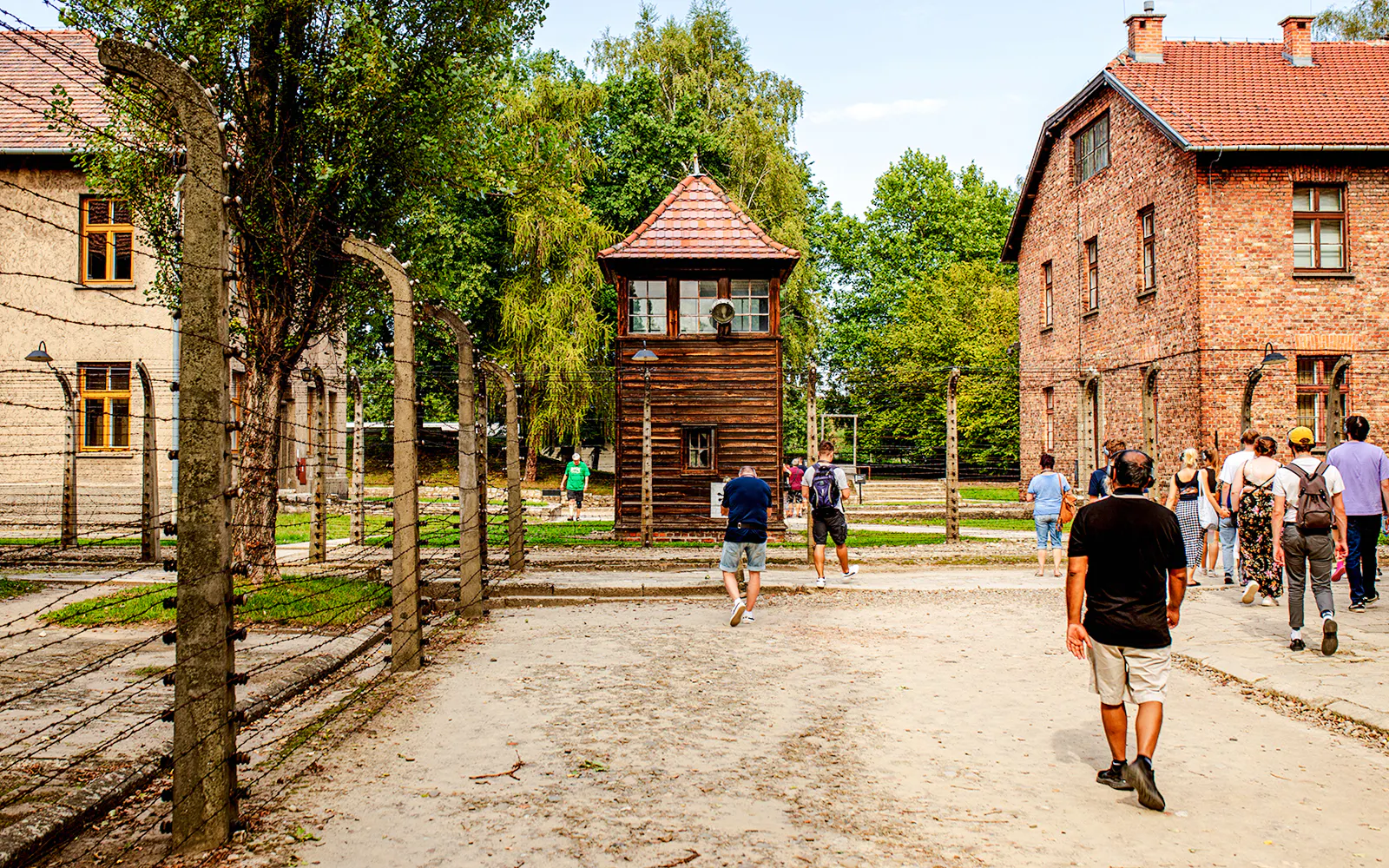 Visitors walking towards a watchtower at Auschwitz-Birkenau during a guided tour.