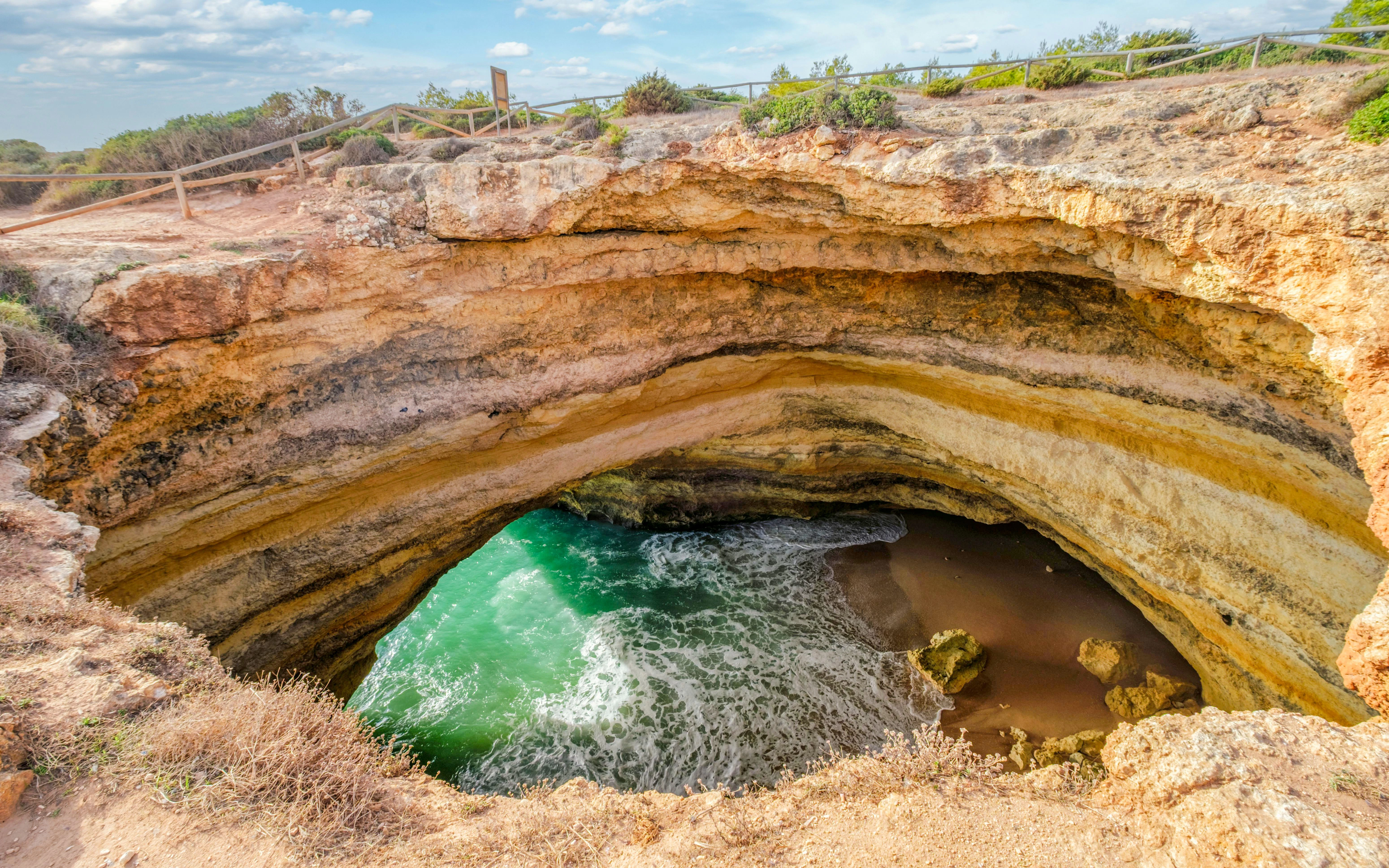 Clifftop view into Benagil Cave, Algarve, Portugal with layered limestone cliffs and Atlantic water.