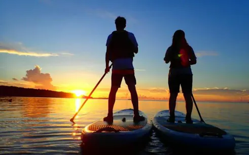 Two people paddleboarding at sunset on Iriomote Island, Okinawa.
