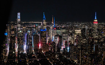 Aerial view of New York City skyline at night with illuminated skyscrapers.