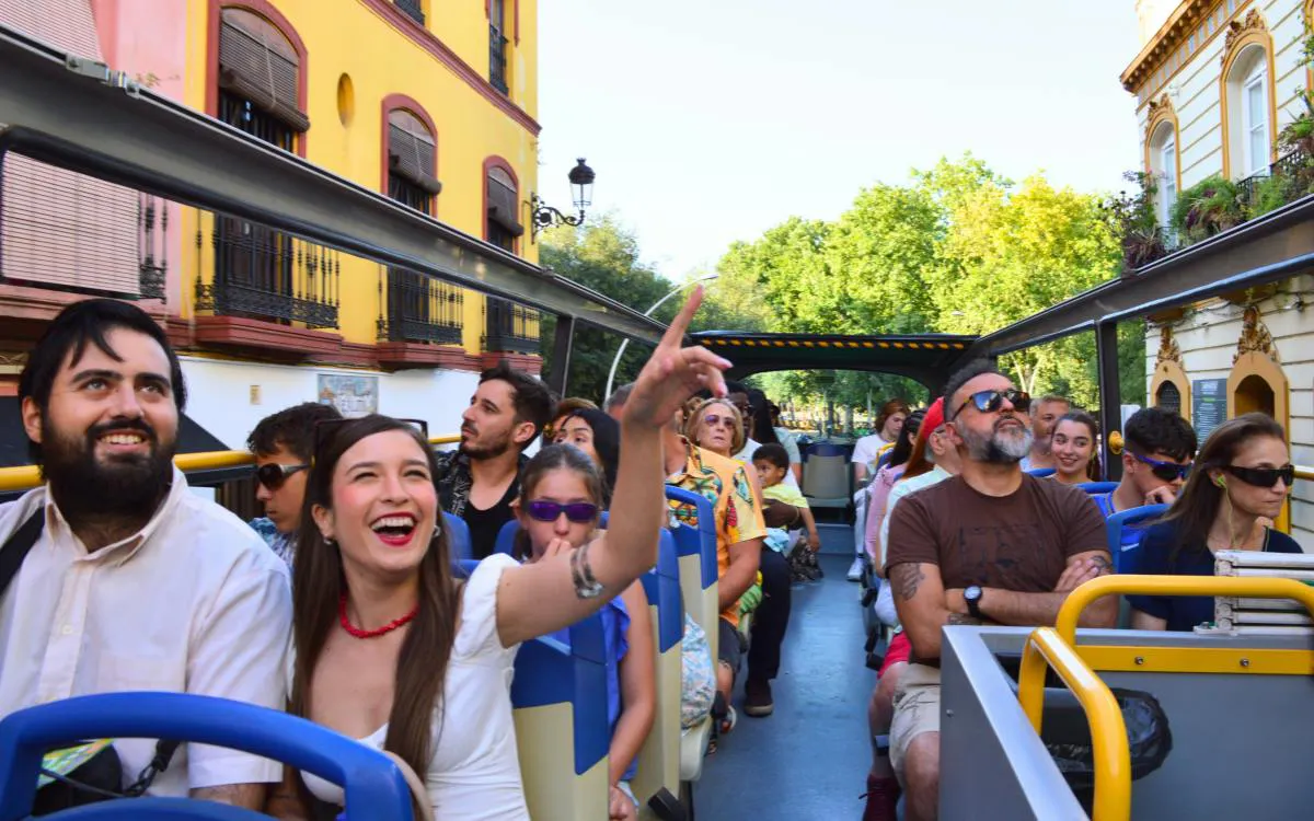 Tourists enjoying a double-decker bus tour in Seville, passing colorful buildings.