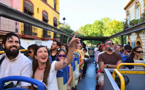 Tourists enjoying a double-decker bus tour in Seville, passing colorful buildings.
