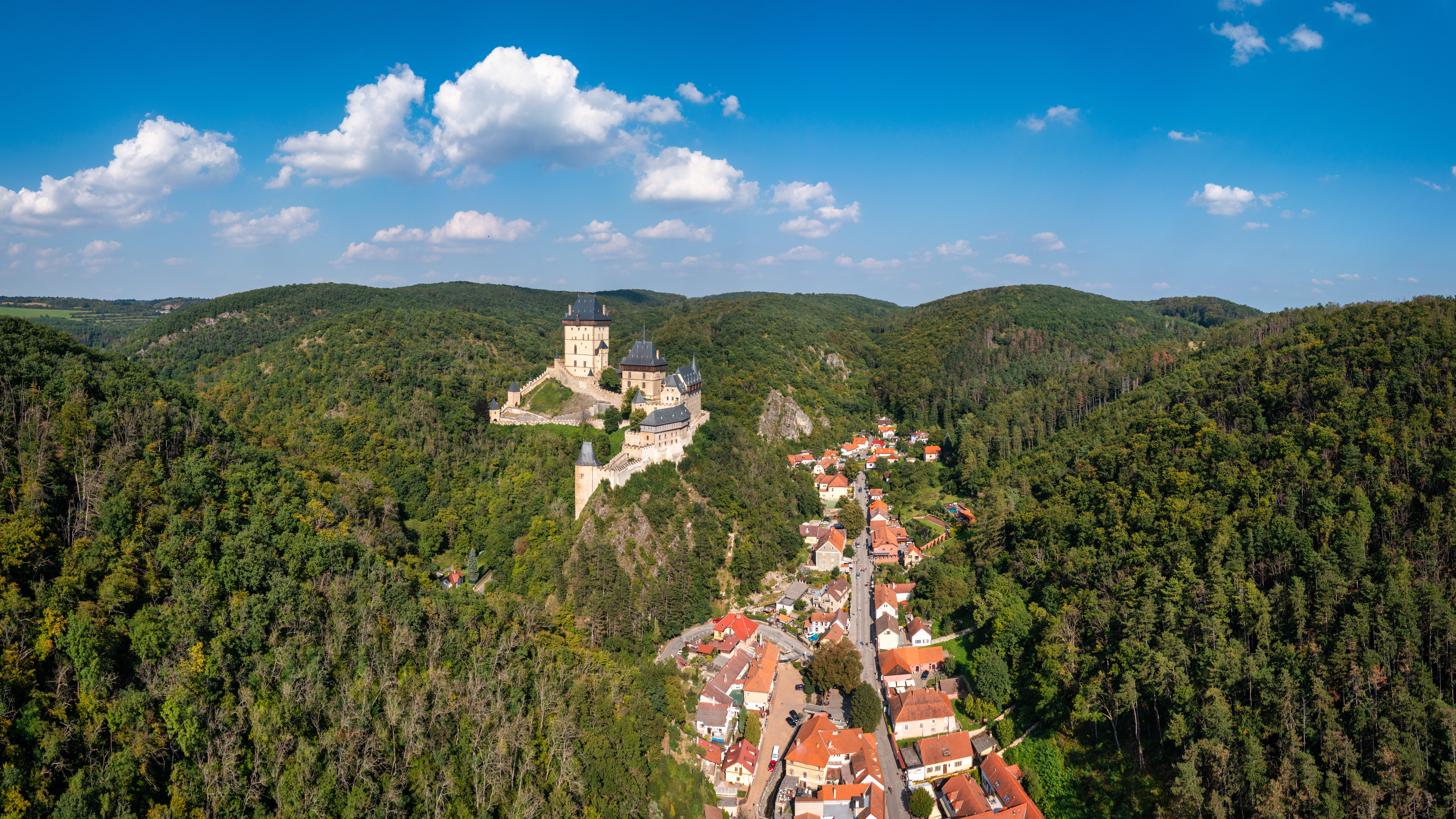 Aerial view of Karlstejn Castle and village surrounded by forested hills.