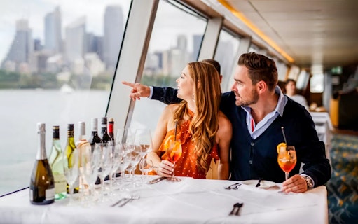 Couple dining on a yacht with Sydney skyline during Sydney to Hobart Yacht Race cruise.
