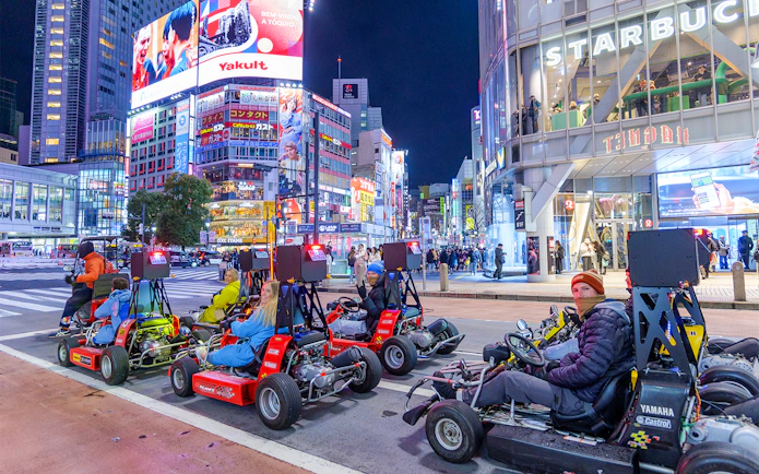 Go-karting at night in Shibuya, Tokyo, with illuminated cityscape and vibrant billboards.