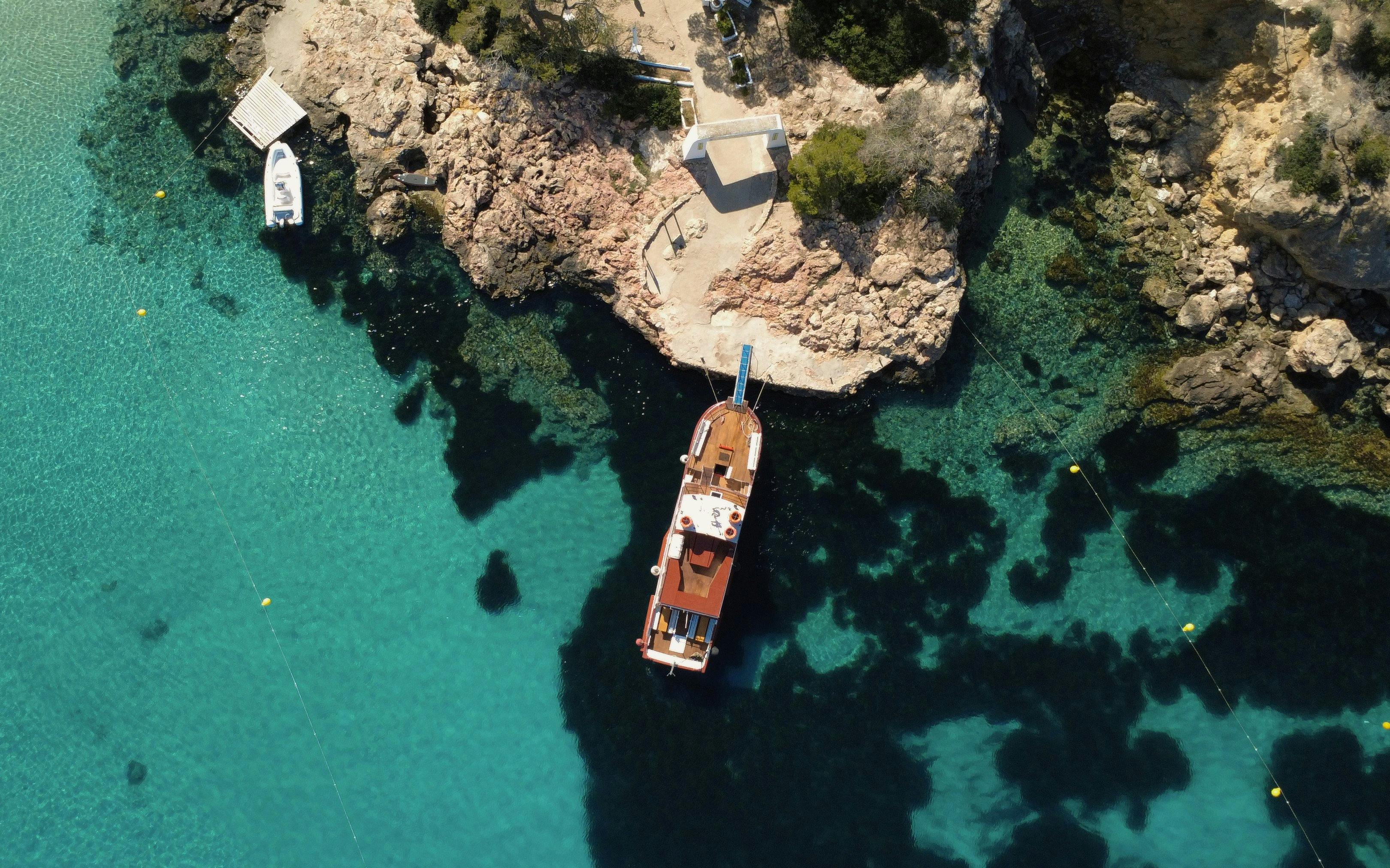 Boat docked at rocky coastline with clear turquoise water, Beach Hopper Cruise Ibiza.