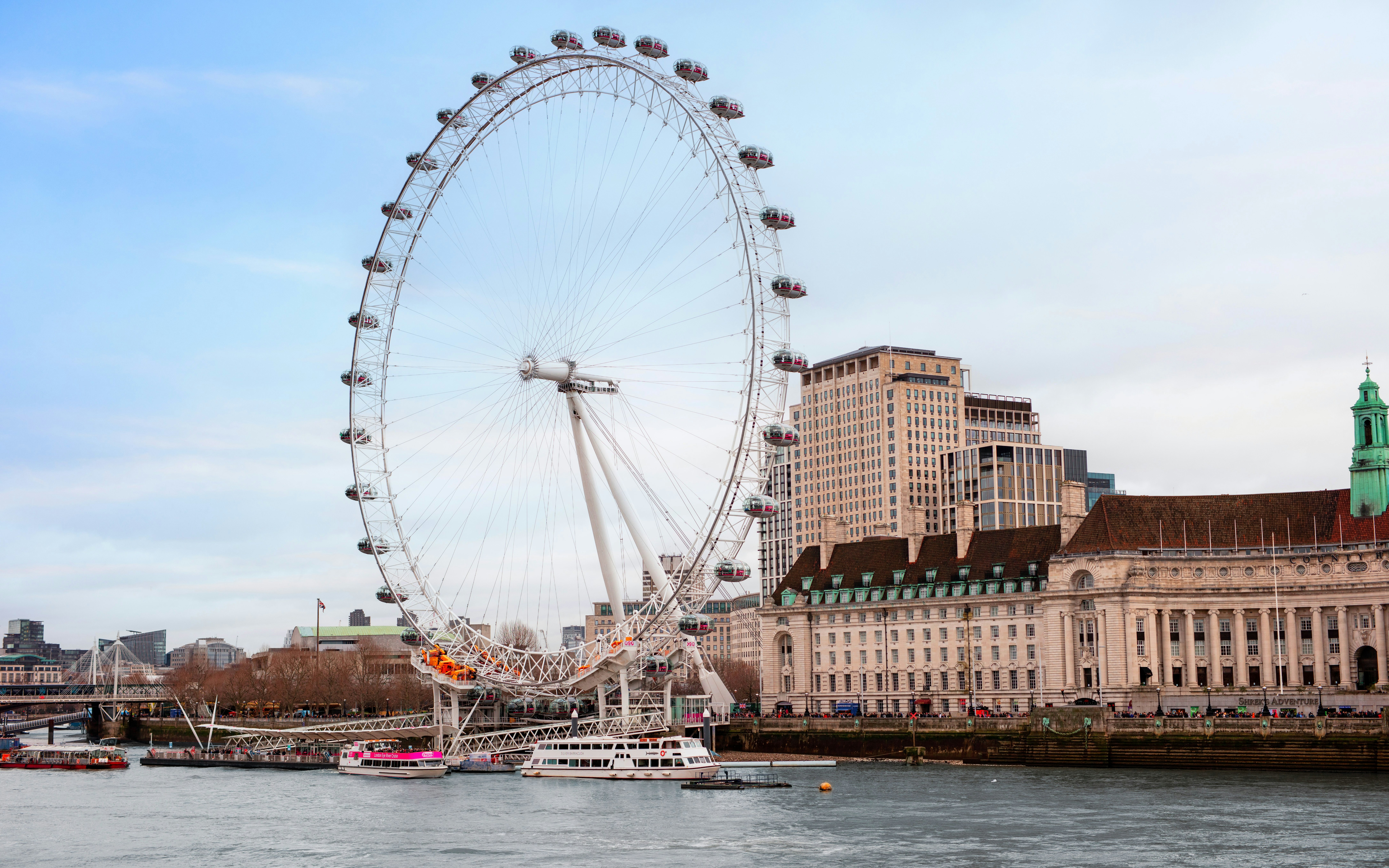 London Eye Ferris wheel on the Thames River with city buildings in the background.