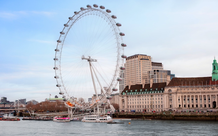 London Eye Ferris wheel on the Thames River with city buildings in the background.