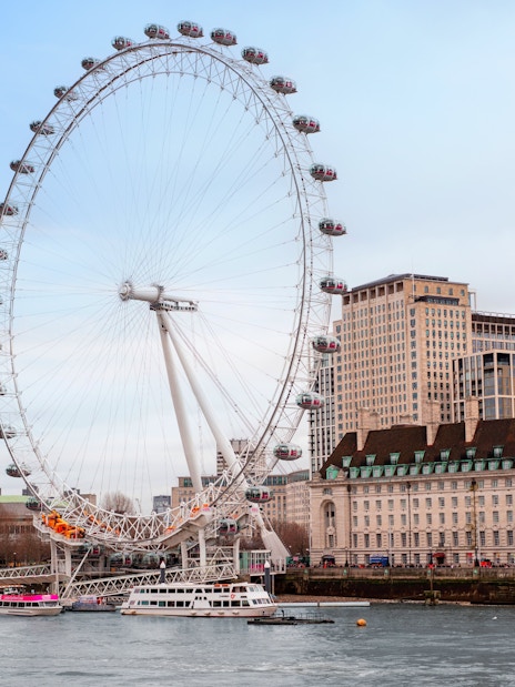London Eye Ferris wheel on the Thames River with city buildings in the background.