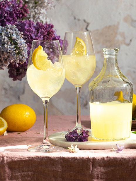 Limoncello bottle with glasses and lemons on a table with flowers in Italy.