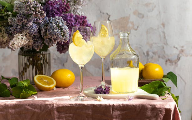 Limoncello bottle with glasses and lemons on a table with flowers in Italy.