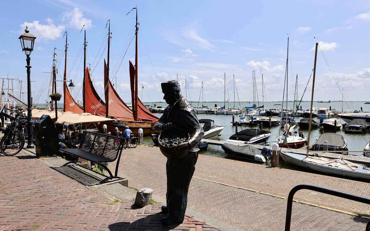 Volendam Harbor with boats and a fisherman statue during daytime.