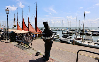 Volendam Harbor with boats and a fisherman statue during daytime.
