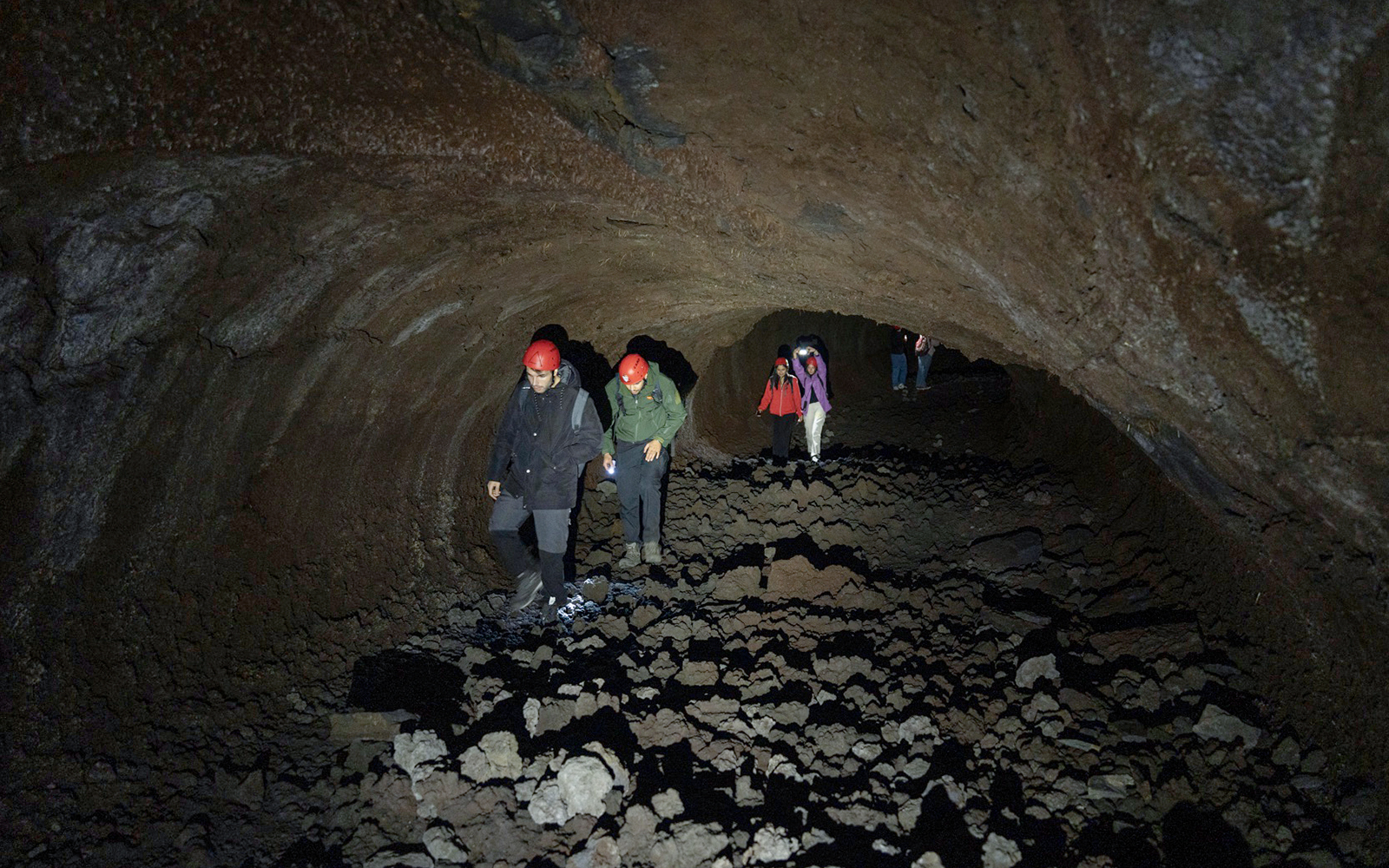 Visitors exploring Mount Etna lava cave with helmets and flashlights.
