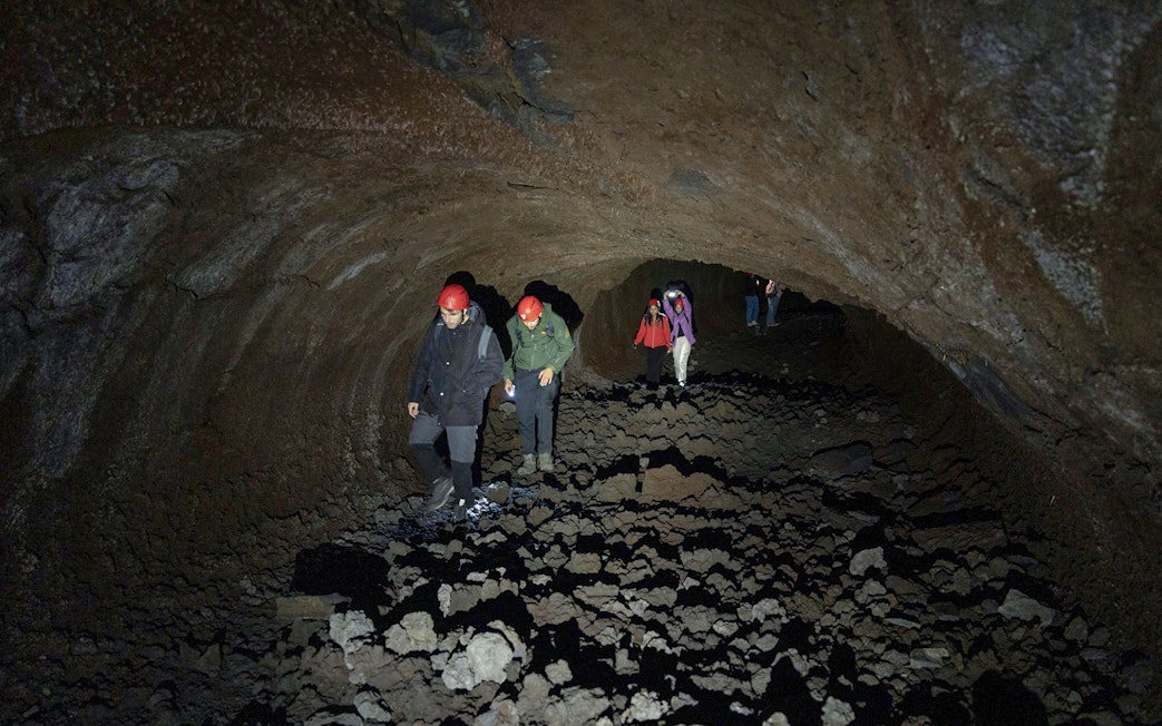 Visitors exploring Mount Etna lava cave with helmets and flashlights.