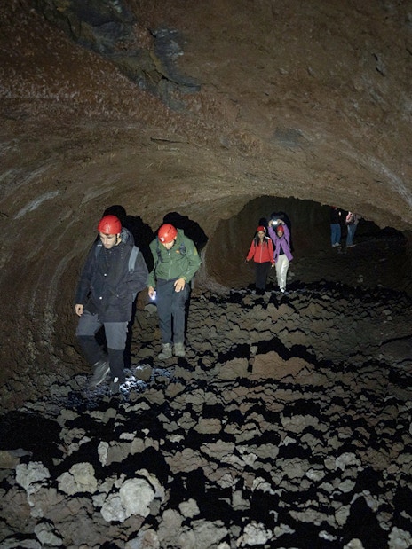 Visitors exploring Mount Etna lava cave with helmets and flashlights.