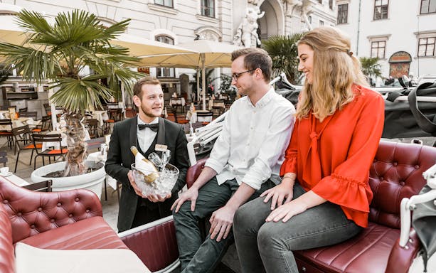 Couple enjoying a city sightseeing tour in an electro vintage car with a waiter serving drinks.