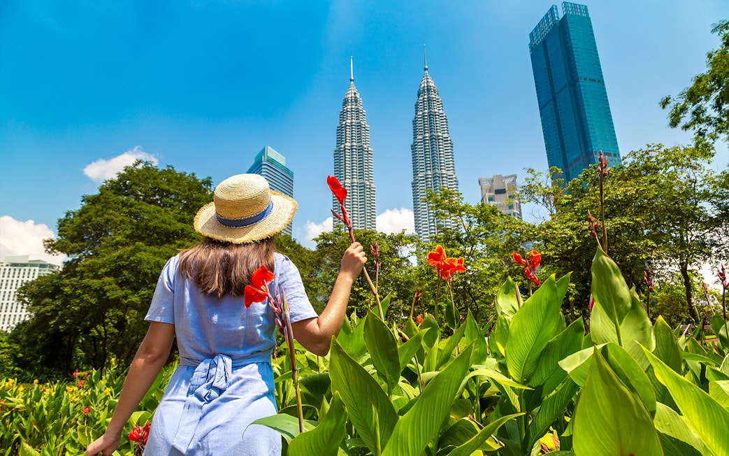Visitor in garden with view of Petronas Twin Towers, Kuala Lumpur.