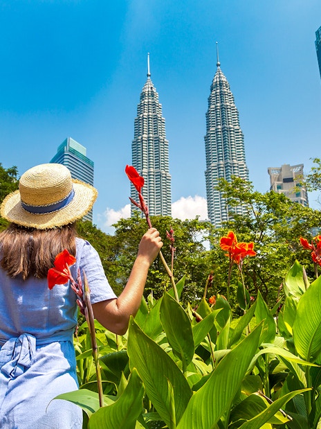 Visitor in garden with view of Petronas Twin Towers, Kuala Lumpur.