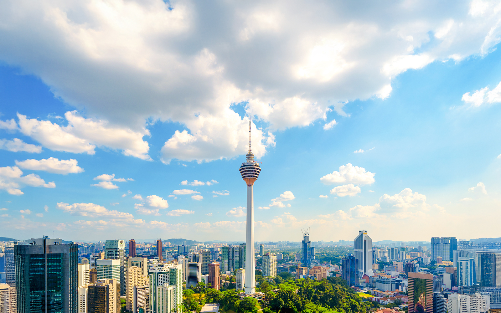 KL Tower rising above Kuala Lumpur skyline under a blue sky.