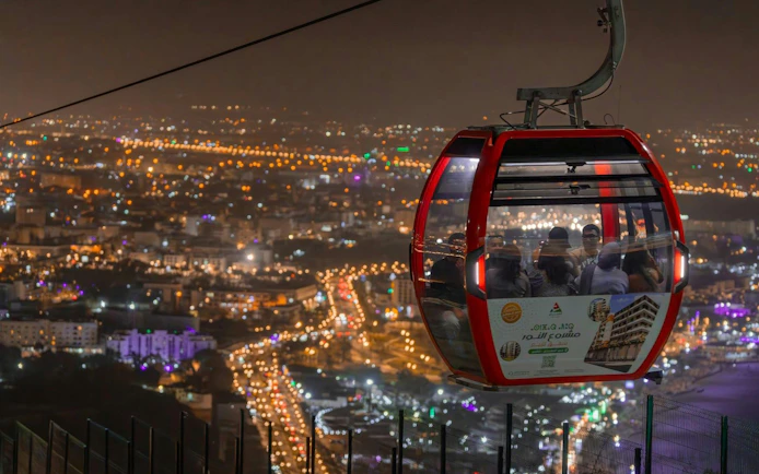 Nighttime view of a cable car over a cityscape with illuminated streets below.