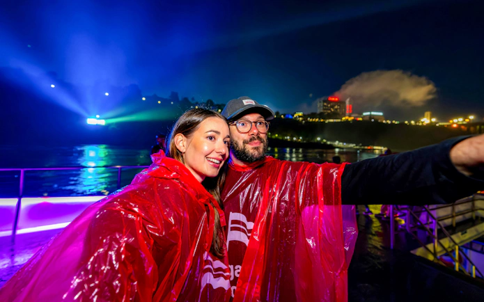 Couple in red ponchos on Niagara Falls fireworks boat cruise at night.