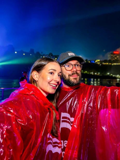 Couple in red ponchos on Niagara Falls fireworks boat cruise at night.