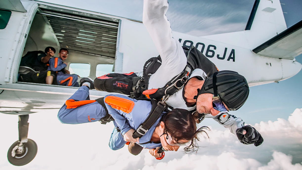 Tandem skydive jump from a plane over a cloud-filled sky.