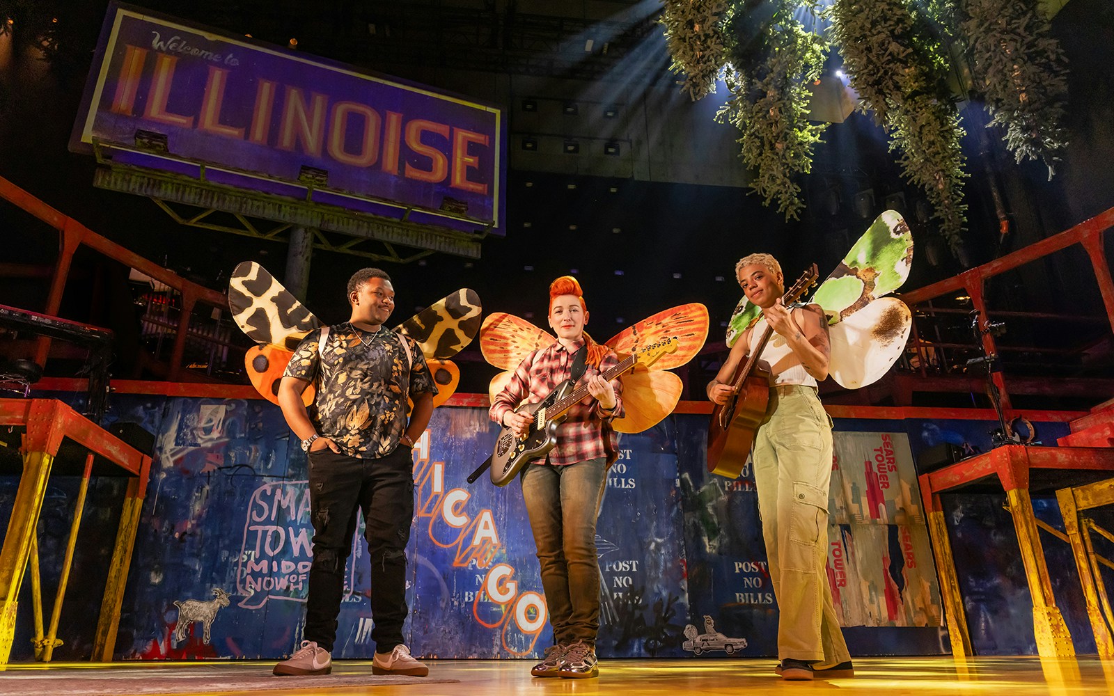 Performers with butterfly wings on stage under "Welcome to Illinoise" sign.
