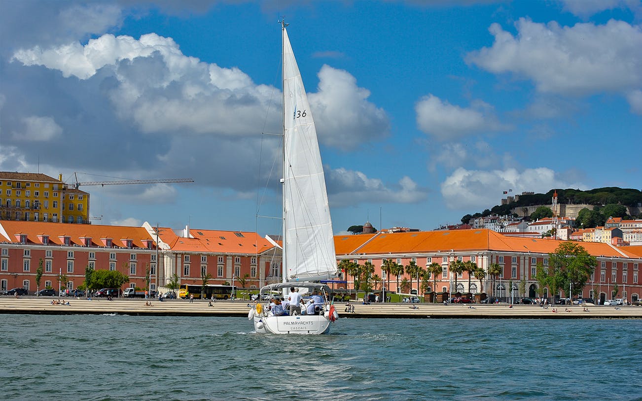 Sailboat on Tagus River with Lisbon's colorful buildings in the background.
