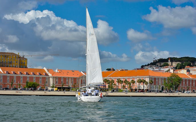 Sailboat on Tagus River with Lisbon's colorful buildings in the background.