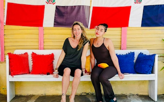 Women sitting on a bench with colorful cushions at a craft market in Punta Cana.