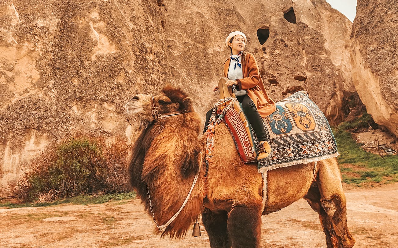 Person riding a camel in Cappadocia with rock formations in the background.
