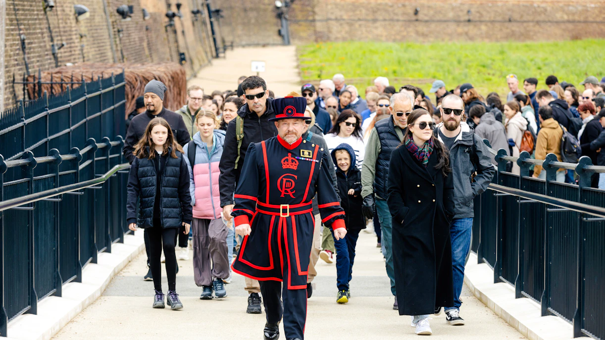 Group of tourists on a guided tour at the Tower of London led by a Beefeater.