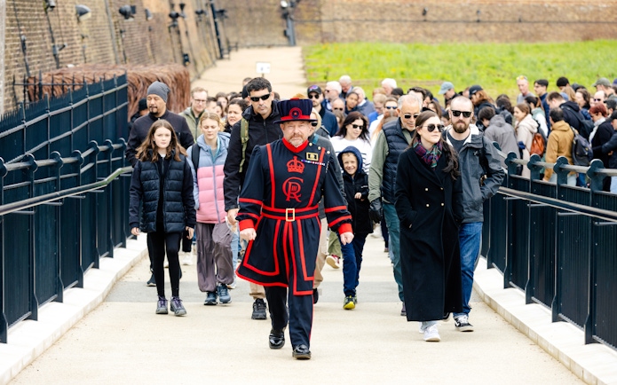 Group of tourists on a guided tour at the Tower of London led by a Beefeater.