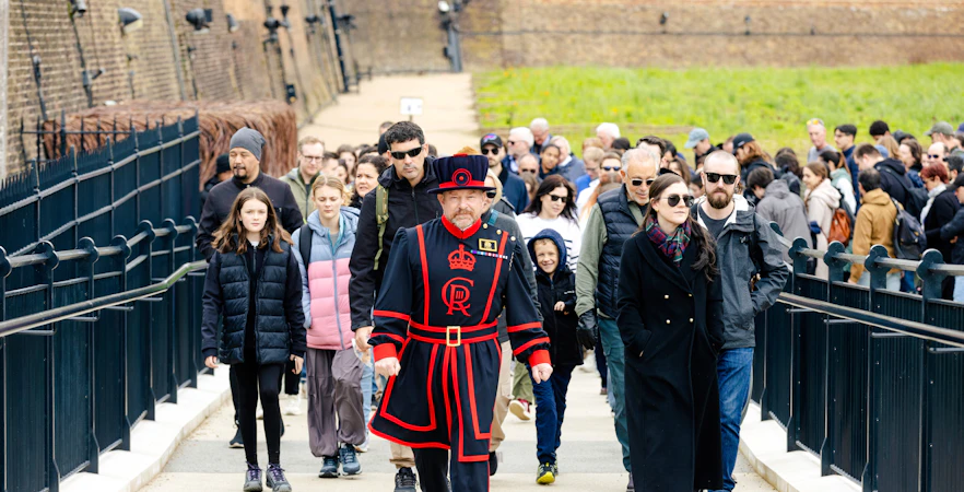 Group of tourists on a guided tour at the Tower of London led by a Beefeater.