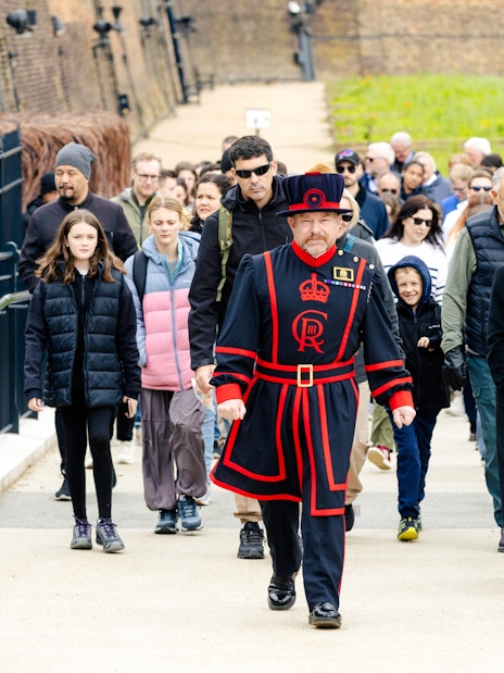 Group of tourists on a guided tour at the Tower of London led by a Beefeater.