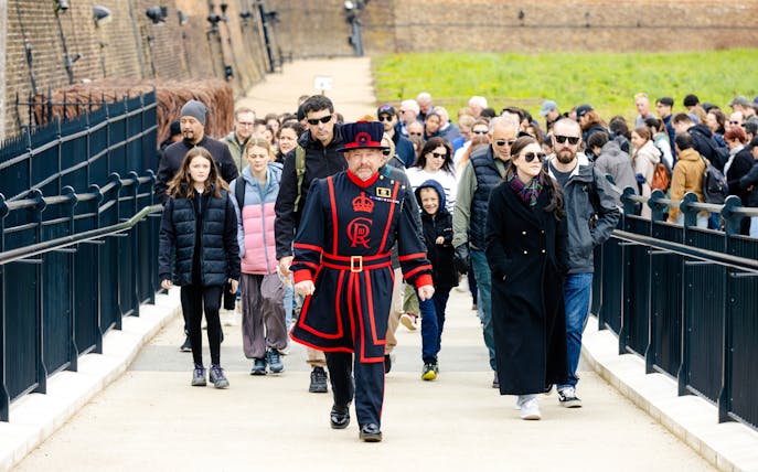Group of tourists on a guided tour at the Tower of London led by a Beefeater.